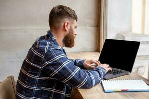 giovane uomo chat attraverso netbook durante opera rompere nel caffè negozio, maschio seduta nel davanti Aperto il computer portatile computer con vuoto copia spazio schermo. foto