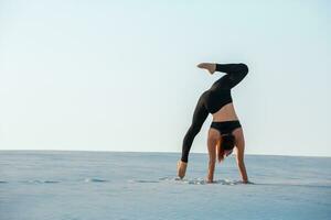 giovane donna praticante inversione equilibratura yoga posa handstand su sabbia. foto