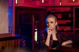 giovane bella donna nel un' camicia nel un' gabbia Fumo un elettronico sigaretta a il Vape bar foto