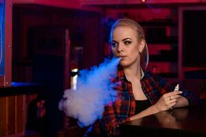 giovane bella donna nel un' camicia nel un' gabbia Fumo un elettronico sigaretta a il Vape bar foto