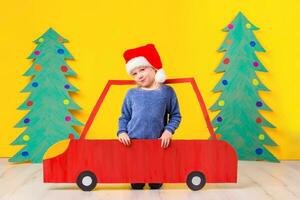 bambino con Natale cappello guida un' auto fatto di cartone. Natale concetto. nuovo anni vacanze. foto