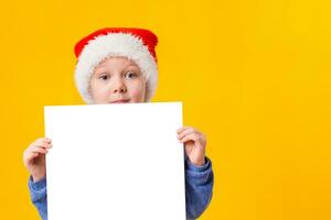 carino poco ragazza nel Santa Claus cappello con un' bianca vuoto carta foglio. Natale, natale, nuovo anno, inverno, le persone, annuncio, vendita concetto. foto