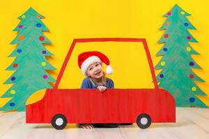 bambino con Natale cappello guida un' auto fatto di cartone. Natale concetto. nuovo anni vacanze. foto