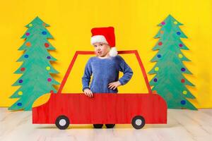 bambino con Natale cappello guida un' auto fatto di cartone. Natale concetto. nuovo anni vacanze. foto