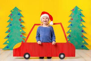 bambino con Natale cappello guida un' auto fatto di cartone. Natale concetto. nuovo anni vacanze. foto