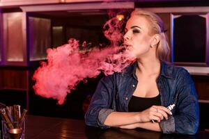giovane bella donna Fumo un elettronico sigaretta a il Vape bar foto