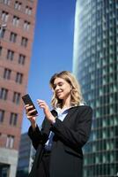 ritratto di riuscito donna d'affari avendo un' telefono conversazione nel senza fili cuffia, a piedi su strada. aziendale donna con smartphone nel città centro foto