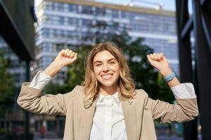 contento sorridente commessa nel beige completo da uomo, celebra sua risultato, trionfante, fabbricazione cazzotto pompa e guardare eccitato su strada di attività commerciale centro foto