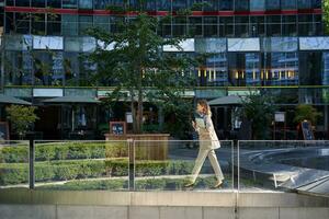 silhouette di giovane attività commerciale donna nel beige completo da uomo, a piedi nel città centro, in posa vicino ufficio edifici, andando per opera foto