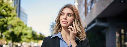 vicino su ritratto di sorridente commessa, riuscito femmina manager avendo Telefono chiamata, risposta telefono e a piedi su strada foto