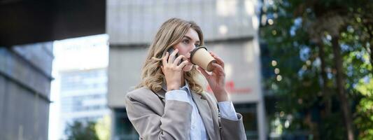 donna d'affari a piedi nel città centro, potabile caffè e parlando su mobile Telefono foto