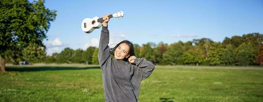 positivo bellezza ragazza con ukulele, danza e sensazione libertà, guardare emozionato, trionfante e festeggiare foto