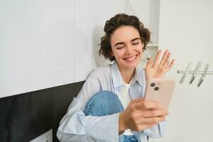 contento sorridente ragazza, detto Ciao per un' amico su video Chiacchierare, onde a smartphone app, si connette per in linea conversazione su sua Telefono foto