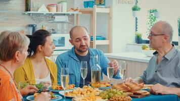 esteso famiglia interagendo mentre avendo un' pasto a cenare tavolo nel il cucina. Multi generazione, quattro le persone, Due contento coppie parlando e mangiare durante un' buongustaio cena, godendo tempo a casa. foto