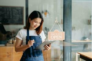 giovane femmina sospeso un' benvenuto cartello nel davanti di un' caffè negozio. bellissimo cameriera o hostess Tenere un' tavoletta preparazione nel un' ristorante. foto