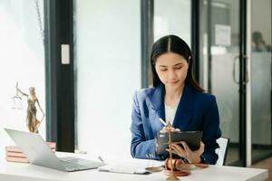 giustizia e legge concetto. asiatico donna avvocato Lavorando e giudice nel un' aula il martelletto, Lavorando con tavoletta e il computer portatile foto