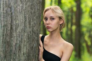 bellissimo ragazza sbirciando su a partire dal dietro a un' albero nel il foresta foto