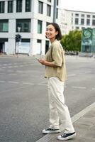 auto condivisione e tecnologia. giovane asiatico donna in attesa per Taxi vicino strada, Tenere smartphone, ordine auto nel applicazione foto