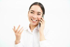 ritratto di asiatico aziendale donna, donna d'affari parla su mobile Telefono, ha conversazione al di sopra di cellulare, A proposito di su telefono, bianca sfondo foto