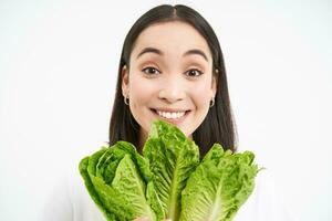 salutare cibo e vegano stile di vita. vicino su ritratto di sorridente asiatico donna, sembra felice, Spettacoli sua viso con lattuga, mangia cavolo, bianca sfondo foto