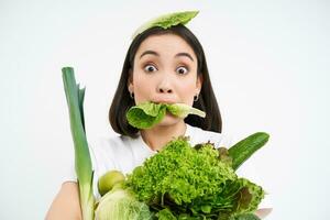 vicino su ritratto di asiatico ragazza sgranocchiare lattuga foglia, Tenere verde oranico la verdura, conduce salutare stile di vita con nutriente cibo, bianca sfondo foto