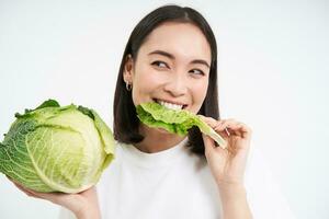 vicino su di carino coreano donna, mangiare cavolo, su dieta, Tenere lattuga, isolato su bianca sfondo foto