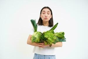 salutare vegano stile di vita. contento asiatico donna sembra a sua preferito la verdura, Tenere cavoli, lattuga e verde biologico cibo, bianca sfondo foto