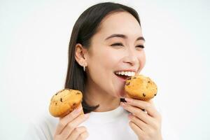 vicino su ritratto di felice, bellissimo sorridente donna, mangiare Pasticcino cupcake, piace forno, bianca sfondo foto