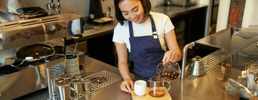 barista nel bar scrosciante filtro caffè, birra e preparazione ordine dietro a contatore, indossare blu grembiule foto