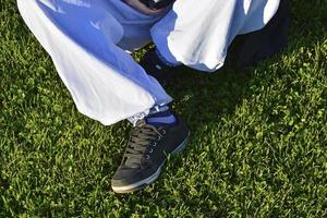 gambe di una ragazza adolescente in blue jeans. la ragazza è seduta sull'erba del campo di calcio. foto