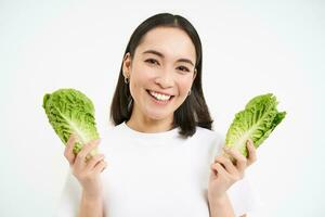 contento coreano donna vegetariano, sorridente e mostrando cavolo, mangiare lattuga su dieta, conduce attivo stile di vita, bianca sfondo foto