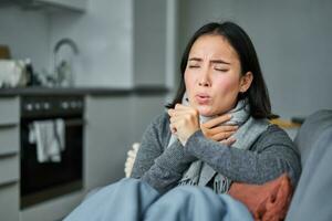 malato coreano donna tosse e sensazione male, smorfie, ha influenza, tosse freddo o influenza, soggiorno a casa foto