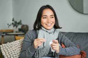 sorridente asiatico donna Tenere termometro e guardare lieto, sensazione meglio dopo freddo, avuto sbarazzarsi di febbre, ha normale temperatura foto