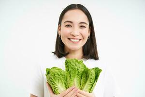 vegetariano nutrizione. sorridente contento giovane donna sembra a sua se stesso cresciuto cavolo, mangiare lattuga, bianca sfondo foto