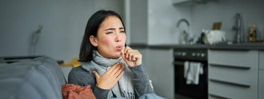 malato coreano donna tosse e sensazione male, smorfie, ha influenza, tosse freddo o influenza, soggiorno a casa foto