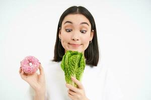 salutare pulito disintossicazione mangiare concetto. vegetariano, vegano, crudo concetto. Immagine di asiatico ragazza sceglie salutare cavolo verdura anziché di rosa smaltato ciambella foto