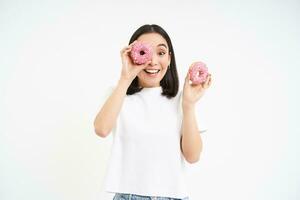 bellissimo giovane donna mangiare delizioso smaltato ciambelle, Tenere Due rosa ciambelle e sorridente, bianca sfondo foto