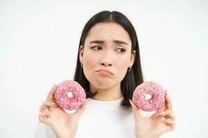 irritato singhiozzando ragazza cant mangiare Rifiuto cibo, Spettacoli delizioso smaltato ciambella, vuole per mordere, bianca sfondo foto