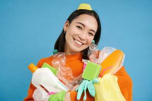 ritratto di sorridente coreano ragazza, Tenere smistato spazzatura per raccolta differenziata, sembra felice, si preoccupa per natura e ambiente, blu sfondo foto