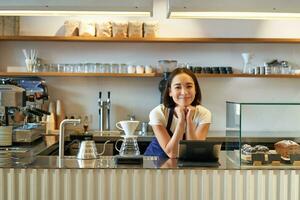 piccolo attività commerciale proprietari. sorridente asiatico ragazza barista, in piedi a contatore con filtro caffè birra kit e pos terminale, bar e persone concetto foto