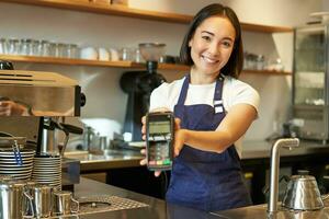 sorridente asiatico barista, caffè negozio personale dà voi credito carta macchina, in lavorazione pagamento con pos terminale, Lavorando nel bar foto