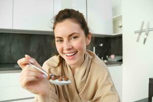 vicino su di bellissimo donna alimentazione voi cereali, avendo prima colazione con latte, sorridente e ridendo, pendente su cucina piano di lavoro foto