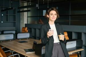 Immagine di donna nel conferenza camera. donna d'affari nel completo da uomo, bevande sua caffè e detiene smartphone, in attesa per incontro per inizio nel ufficio foto