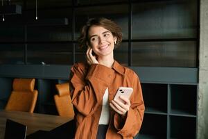 giovane donna, ufficio dipendente, Lavorando nel conferenza camera, rispondendo per Telefono chiamata con senza fili cuffia, Tenere smartphone foto