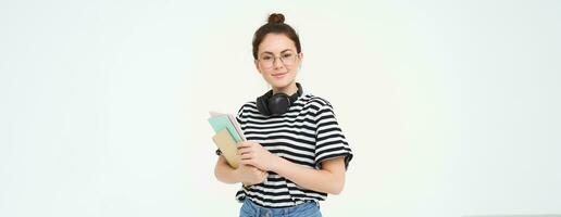 giovane donna con i Quaderni, libri e studia Materiale, in posa al di sopra di bianca sfondo, indossa cuffie al di sopra di collo foto