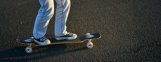 ritagliata tiro di gambe su longboard. pattinatore ragazza equitazione sua skateboard su strada. femmina adolescente su incrociatore foto