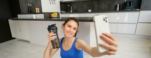 benessere e gli sport. bellissimo giovane donna assunzione autoscatto su smartphone, fare fitness formazione a partire dal casa, bevanda acqua, soggiorni idratato e fare esercizi foto