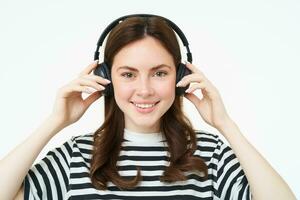 ritratto di donna, sorridente, indossare senza fili cuffia, ascoltando musica, studiando nel auricolari, in piedi isolato al di sopra di bianca sfondo foto