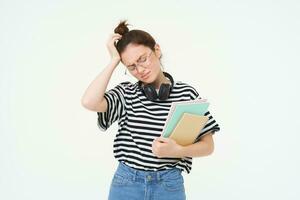 deluso giovane donna, guardare stanco o rovesciato, indossare occhiali, Tenere studia Materiale, documenti e i Quaderni, sta al di sopra di bianca sfondo foto