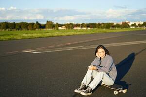 pattinatore ragazza si siede su sua skateboard su strada, utilizzando smartphone, chat su mobile App foto